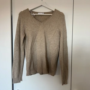 Beige stickad tröja  - Säljer en stilren beige stickad tröja från vila med v-ringning. Tröjan har långa ärmar och ribbade muddar vid ärmslut och nederkant.🤍