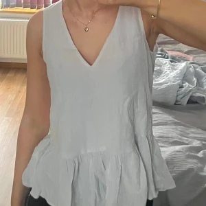 Vit ärmlös blus med knytning - Säljer en stilren vit blus med v-ringning och volangdetalj i nederkant. Blusen är ärmlös och har en snygg öppen rygg med knytning. Perfekt för varma dagar eller sommaren💗