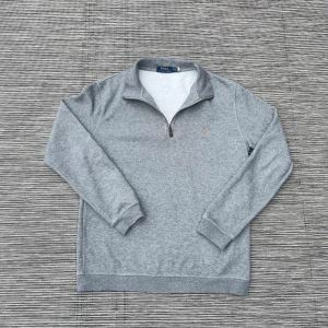 Grå tröja med dragkedja från Polo Ralph Lauren - Säljer en stilren grå tröja från Polo Ralph Lauren med halv dragkedja och broderad logga på bröstet. Tröjan är i storlek Medium M. Tröjan har långa ärmar och är tillverkad i ett mjukt material.🙌🙌 Om du har några frågor är det bara att höra av dig👍