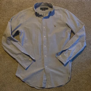 Blå skjorta från Ralph Lauren - Säljer just nu en snygg blå skjorta från Ralph Lauren i slim fit. Skjortan har långa ärmar och är dekorerad med det klassiska broderade logotypen på bröstet. Perfekt för en stilren look. Ny pris runt 1600 mitt pris 649. Skicket är 9/10. Säljer då den har blivit lite för liten. Skulle passa någon runt 173-183. Skriv för fler frågor eller bilder. Passar perfekt till jeans eller till linnebyxor. Priset kan alltid diskuteras vid snabb affär.🤩 Färgen syns i bild 4.
