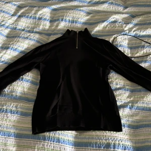 Svart tröja med dragkedja från Jack & Jones - Säljer en stilren svart tröja från Jack & Jones med dragkedja vid halsen. Tröjan har långa ärmar och ribbade detaljer vid ärmslut och nederkant. Perfekt för en stillig look