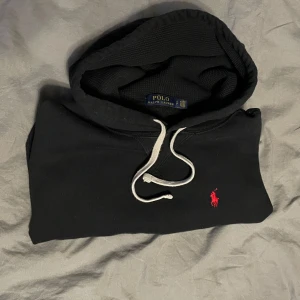 Svart hoodie från Ralph Lauren - Säljer en stilren svart hoodie från Ralph Lauren med det klassiska röda logotypen på bröstet. Skick 9/10 (äkta) hör av dig för fler bilder.