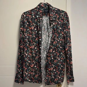 Blommig skjorta från Grand Frank - Snygg blommig skjorta från Grand Frank i en mörk färgton med färgglada blommor. Skjortan har en slim fit passform och långa ärmar, perfekt för en stilren look.