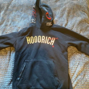 Svart hoodie från Hoodrich - Säljer en svart hoodie från Hoodrich med tryck på både fram- och baksidan. Hoodien har en stor ficka framtill och en justerbar huva. Perfekt för en avslappnad stil.