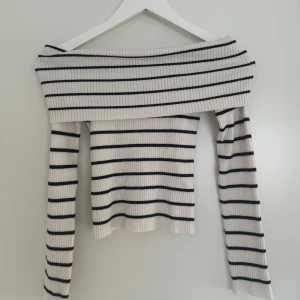 Randig offshoulder tröja från H&M - Säljer en stilren randig offshoulder tröja från H&M. Tröjan är ribbad och har långa ärmar, perfekt för en trendig look. Den är vit med svarta ränder och passar bra till både jeans och kjol. Perfekt för vår och sommar!