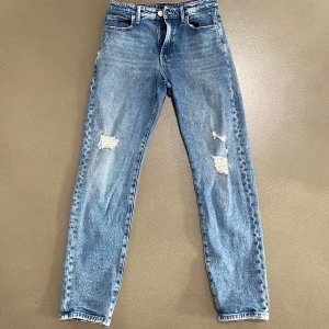 Blå jeans från Tommy Hilfiger - Snygga blå jeans från Tommy Hilfiger med slitna detaljer på framsidan. De har en klassisk femficksdesign och en knappgylf. Perfekta för en avslappnad stil.