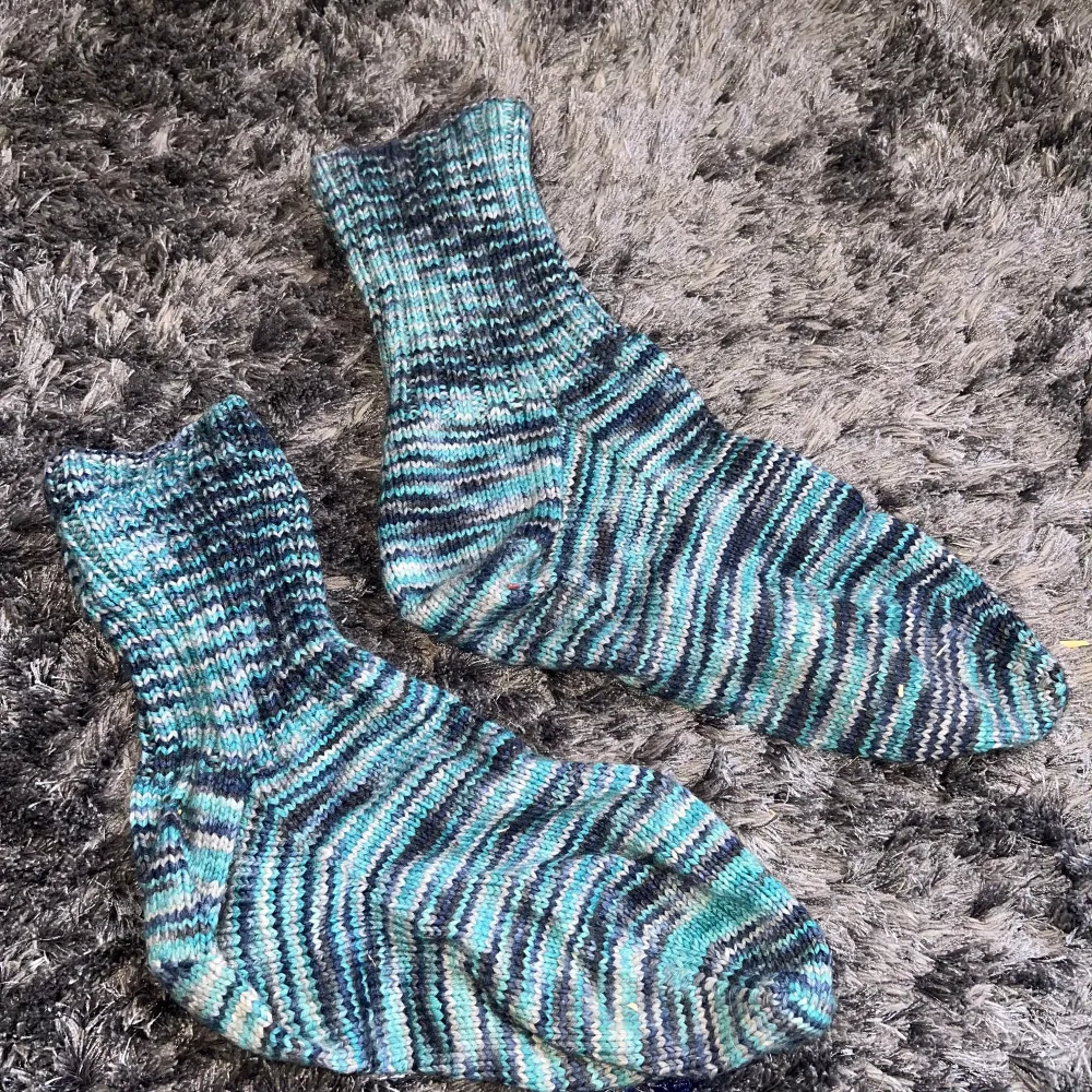 Säljer ett par mysiga stickade strumpor med randigt mönster i olika nyanser av blått och grönt. Perfekta för att hålla fötterna varma under kalla dagar. Strumporna har en ribbad kant upptill för extra komfort.. Muu.
