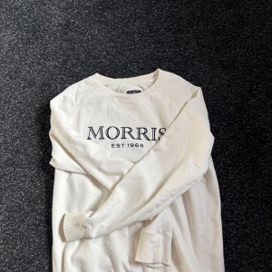Vit tröja från Morris - Vit tröja från Morris med tryck 'Morris Est 1968' på framsidan. Tröjan har långa ärmar och en rund halsringning. Perfekt för en avslappnad stil. Storlek Medium