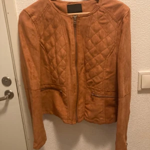 Brun mockajacka från Amisu stl 38 - Snygg brun mockajacka från Amisu med quiltade detaljer och dragkedja framtill. Jackan har en stilren design med långa ärmar och två fickor med dragkedjor. Perfekt för en trendig look! NY!!!