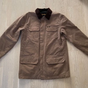 Wrangler jacka - Brun/beige canvas jacka från Wrangler storlek L (lite större i storleken). Varm och bra med förvaring. Liten nästintill osynlig rispa på vänster skuldra (hör av er för fler bilder) Krage i manchester.