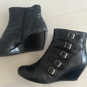 Svarta klackade boots från Vagabond - svarta boots från Vagabond med kilklack och dekorativa spännen. Skorna har en dragkedja på sidan för enkel på- och avtagning. Storlek 36, bra skick!