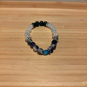 Färgglatt armband med pärlor - Snyggt armband med en mix av färgglada pärlor i blått, vitt och grönt. Armbandet har en elastisk tråd för enkel passform och inkluderar glittriga detaljer som ger en extra touch av stil.