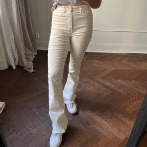 Vita högmidjade byxor från Massimo dutti - Snygga vita högmidjade byxor med en klassisk bootcut-stil. Perfekta för en stilren look och kan matchas med olika toppar. Byxorna har en dragkedja och knappar framtill.