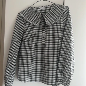 Rutig blus från VRS - Säljer en stilren rutig blus från VRS i svart och vit. Blusen har långa ärmar och knappar framtill. Den har en klassisk krage och ett tidlöst mönster som passar perfekt för olika tillfällen.