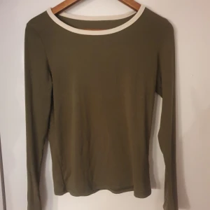 Olivgrön långärmad tröja med vit kant - Säljer en stilren olivgrön tröja med lång ärm och vit kant vid halsringningen. 