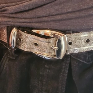 Glittrigt silverfärgat bälte från Nanni - Snyggt glittrigt bälte i silver från Nanni, tillverkat i Italien. Bältet har en stilren design med en silverfärgad spänne och flera justerbara hål för perfekt passform. Perfekt för att ge din outfit en extra touch av glamour. Notera defekt på bild tre, hittat två ställen där de blivit sådär.