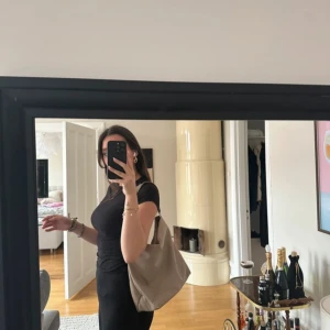 CW Beige axelväska med dragkedja - Snygg beige axelväska i syntetmaterial med dragkedja och stilrena detaljer. Väskan har ett rymligt inre med mönstrat foder och flera fack för enkel organisering. Perfekt för att bära med sig det nödvändigaste med stil. En liten skavank på axelbandet (se bild)