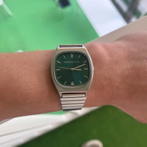 Retro klocka från Retrodiction - Säljer en snygg retroinspirerad klocka från Retrodiction. Den har en grön urtavla och ett stilrent silverfärgat armband i rostfritt stål. Perfekt för både vardag och fest! Klockan har datumvisning och är vattentålig. Passar dig som gillar en klassisk men ändå modern stil.