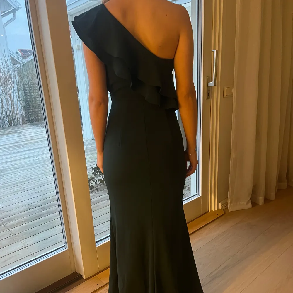 Elegant mörkgrön långklänning med en axel och volangdetaljer. Perfekt för en stilfull kväll.. Mekot.