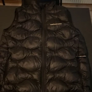 Svart dunväst från Peak Performance - Snygg svart dunväst från Peak Performance med dragkedja framtill. Perfekt för kyliga dagar och ger en stilren look. Västen har en quiltad design som ger extra värme och komfort.