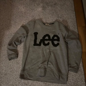 Grå sweatshirt från Lee - Säljer en grå sweatshirt från Lee med deras ikoniska logga i svart på framsidan. Tröjan har långa ärmar och en rund halsringning. Perfekt för en avslappnad stil.