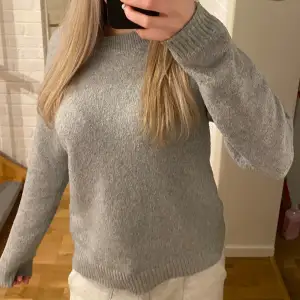 Säljer en mysig grå stickad tröja med långa ärmar och ribbade muddar. Perfekt för kyliga dagar. Passar till både jeans och kjol.