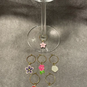 Blommiga glasmarkörer i olika färger - Säljer ett set med sex glasmarkörer i form av blommor. Varje markör har en unik design och färg. Ringen är i guld. Perfekt för att hålla koll på glasen vid festliga tillfällen.🎉🥂⭐️ De är lätta att fästa på glasets fot. Jag driver ett uf företag som heter DrinkRingsUF. På min sida går det att hitta fler glasmarkörer i andra teman också! Jag tillverkar alla glasmarkörer själv. 