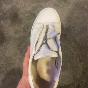 Arigato skor Zip vit Herr - Hej! Säljer dessa snygga vita Axel Arigato skor i bra skick! Använda och det syns men fortfarande mycket liv i sig! Skick enligt bilder! Storlek 42! Skriv för intresse!