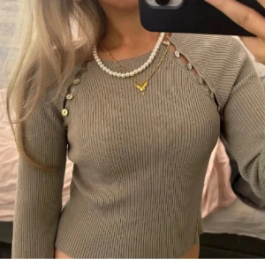 Beige ribbad tröja från Zara - Säljer en stilren beige ribbad tröja från Zara med knappar längs sidorna. Tröjan har långa ärmar och en figurnära passform. Perfekt för en chic och bekväm look.