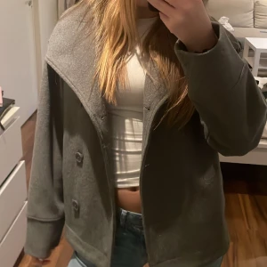 Grå jacka från Gina Tricot - Säljer en stilren grå jacka från Gina Tricot. Jackan har en klassisk design med knappar framtill och långa ärmar. Perfekt för en trendig look.