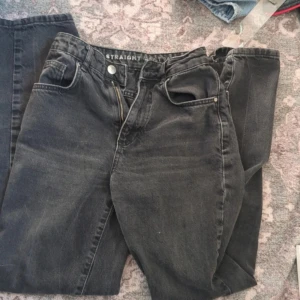 Svarta jeans från Never Denim - Säljer ett par svarta jeans från Never Denim i modellen 90s Straight. De har en klassisk rak passform och är perfekta för en stilren look. Jeansen har en knappgylf och femficksdesign.