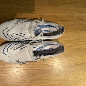 ADIDAS PREDATOR ELITE FOLD-OVER TONGUE FG POLAR VICTORY - VIT/SILVER/BLÅ - Säljer ett par vita adidas predator elite FG, använda 4 gånger på konstgräs. Passade tyvärr inte min fot. Den ända defekten är att de är lite smutsiga annars är de i mycket bra skick.