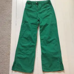 Snygga gröna byxor med vida ben och slitsdetaljer vid fållen. Byxorna har en hög midja och stängs med knapp och dragkedja. Perfekta för en färgglad look! Bara använda några gånger.