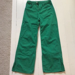 Gröna vida byxor med slits - Snygga gröna byxor med vida ben och slitsdetaljer vid fållen. Byxorna har en hög midja och stängs med knapp och dragkedja. Perfekta för en färgglad look! Bara använda några gånger.