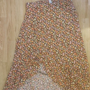 Blommig kjol från Amisu - Säljer en färgglad blommig kjol från Amisu. Kjolen har ett härligt mönster i orange, rosa och gul på en svart bakgrund. Perfekt för en somrig look med sin luftiga design och elastiska midja.