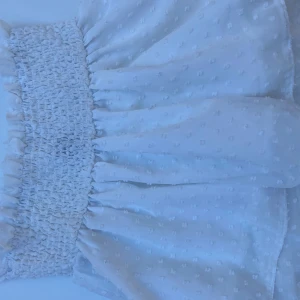 Vit kortkjol med smockdetalj - Söt vit kortkjol med smockdetalj i midjan och ett diskret prickigt mönster. Kjolen har en luftig och voluminös design som ger en romantisk känsla. Fint skick, det som syns igenom är märkeslappen 🩷