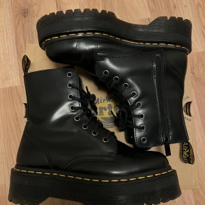 Svarta boots från Dr. Martens - Säljer ett par svarta Dr. Martens Jadon boots i polerat skinn med snörning och dragkedja. De har en robust platåsula med den klassiska gula sömmen. Perfekta för en edgy look!