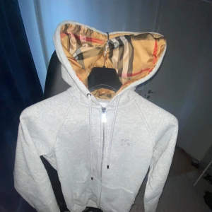 Grå hoodie från Burberry - Säljer en stilren grå hoodie från Burberry med dragkedja och klassiskt mönstrad huva. helt ny pris ligger på 649.