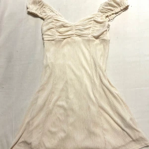 Beige/vit klänning från Gina Tricot - Säljer en söt beige/vit klänning från Gina Tricot med jättefin figurnära passform. Använd endast en gång och finns inga defekter eller tecken på användning