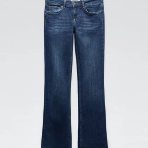 Blå low waist bootcut jeans från Zara - Supersnygga mörkblå low waist bootcut jeans från Zara med klassisk femficksdesign och knappgylf. Jeansen är tillverkade i ett slitstarkt denimtyg. Helt slutsålda och säljs inte längre på Zara! Storlek 32. Något slitna längst ner men inget som man tänker på över huvud taget
