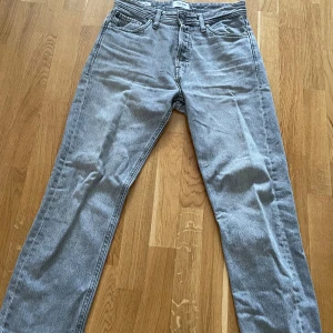 Grå jeans från Jack & Jones - Säljer ett par grå jeans från Jack & Jones med en relaxed passform. De har en klassisk femficksdesign och knappar i midjan. Perfekta för en avslappnad stil.