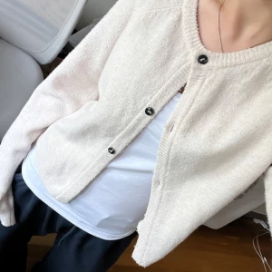 Beige stickad kofta från Lindex - Säljer en beige/ljusrosa stickad kofta från Lindex med rund hals och svarta knappar framtill. Koftan har lång ärm och ribbade muddar vid ärmslut och nederkant. Lite nopprig! 
