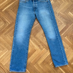 Levi's 501 ljusblå jeans straight fit - Klassiska Levi's 501 jeans i ljusblå tvätt med raka ben och normal passform. Jeansen har fem fickor, knappgylf och är tillverkade i slitstarkt bomullsjeans. Perfekta för en avslappnad och tidlös stil. Storlek 30- 32