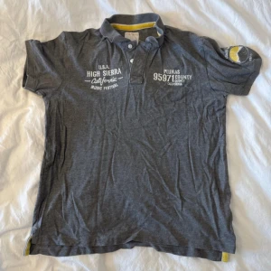 Grå pikétröja från Esprit med broderi - Säljer en grå pikétröja från Esprit med vit broderad text på bröstet och ett coolt broderat märke på ärmen med solmotiv och texten 'Here Comes The Sun'. Tröjan har krage med två knappar och gul detalj på insidan av kragen. Perfekt för dig som gillar avslappnad stil.