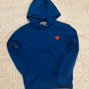 Blå hoodie Comme des Garçons Play - Blå hoodie från Comme des Garçons Play i storlek S. Tröjan har huva, magficka och det ikoniska röda hjärta med ögon broderat på bröstet. | Skick: 9 / 10, sparsamt använd! | Nypris: ~4300 | Vårt pris: 1299 | Storlek: S | Tveka inte att höra av er med funderingar! 