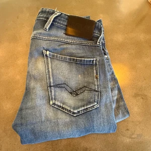 Blå Replay anbass jeans med slitningar  - Tja jag säljer dehär snygga Replay anbass jeansen i modellen midwaist med klassisk femficksdesign och coola slitningar. Jeansen har raka ben och tydliga kontrastsömmar på bakfickorna. De är i storlek W30 L32. Tillverkade i bomull med en skön passform som funkar till allt.
