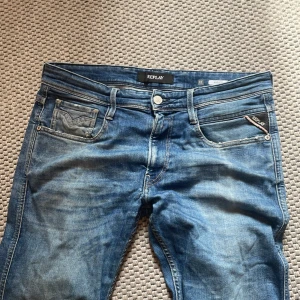 Blå Replay Anbass jeans herr - Säljer ett par snygga Replay Anbass jeans i klassisk blå tvätt. Jeansen har fem fickor, Replay-logga på bakfickan och läderpatch i midjan. De är tillverkade i mjukt jeansmaterial och har en modern passform med lätt slitningar för en cool look.