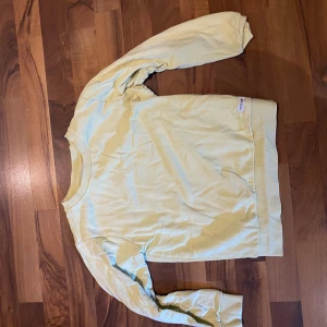 Ljusgul sweatshirt med rund hals - En enkel och clean ljusgul sweatshirt med rund hals och långa ärmar. Tröjan har breda muddar vid ärmslut och nederkant, vilket ger en chill och avslappnad vibe. Perfekt för att matcha med jeans eller mjukisbyxor. Materialet känns mjukt och skönt mot huden.