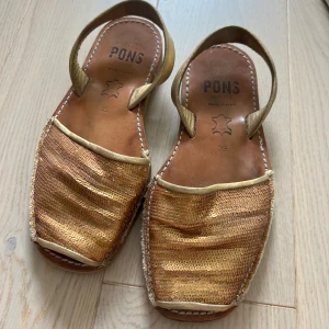 Guldiga Pons sandaler  - Säljer mina sandaler från Pons menorca i guldigt skinn med glittriga paljetter över. Sandalerna är gjorda av äkta skinn och är handgjorda.  Välanvända men inte trasiga någonstans. Väldigt sköna att gå i. Storlek 39. Nypris cirka 1000 kr, mitt pris 350 kr. Köparen står för frakten🫶🏻