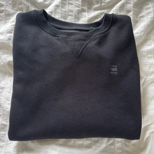 Svart sweatshirt från G-Star RAW - Svart sweatshirt från G-Star RAW med diskret logga på bröstet. Klassisk rund hals och ribbade muddar vid ärmslut och nederkant. Skick: 10/10. Nypris: 1000kr. Skriv för fler frågor.